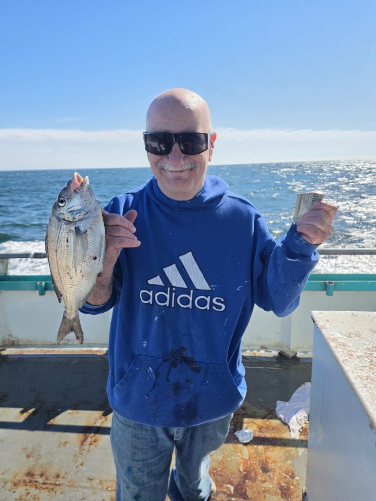 Man in sunglasses holding a fish on a boat with ocean background.