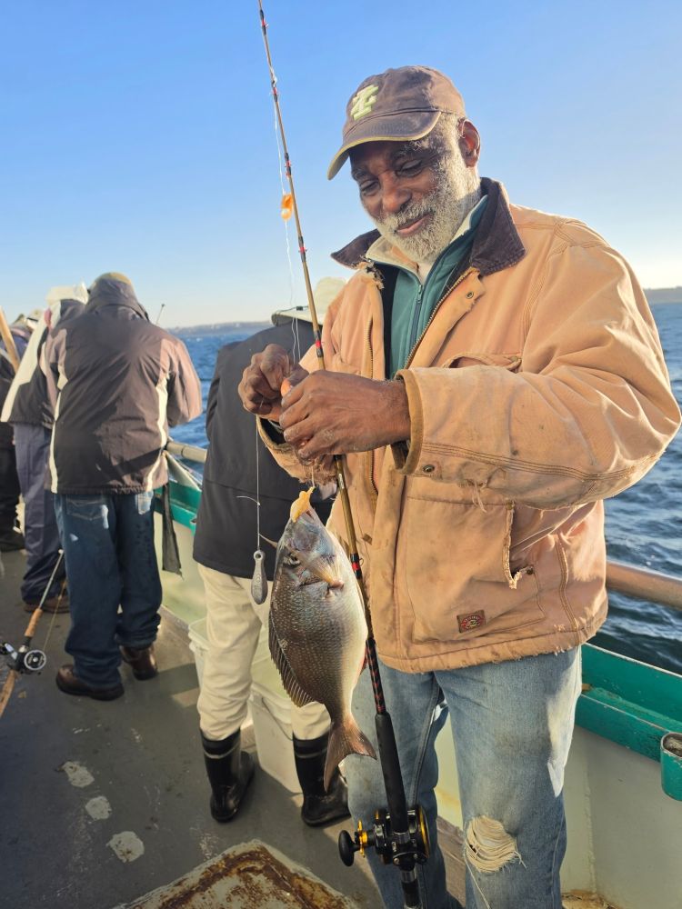 Smiling man on boat holding a fish he caught with a fishing rod.