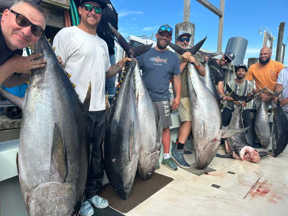 Group of people holding large fish on a dock, smiling at the camera.