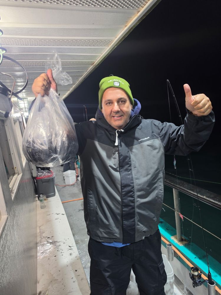Person in a jacket holding a bag of fish on a boat, giving thumbs up.