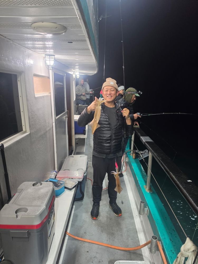 Person on boat holding a small squid, smiling, night fishing scene.