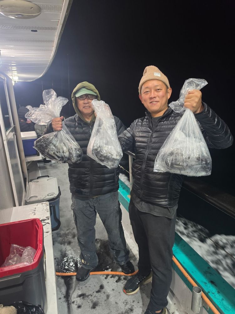 Two people on a boat holding bags of fish at night.
