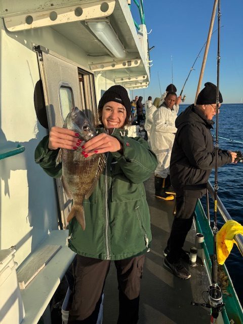 Person in a green jacket holding a fish on a boat with other people.