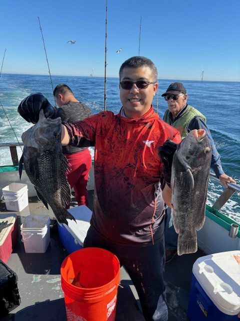 Three people on a boat holding large fish, with a blue ocean in the background.