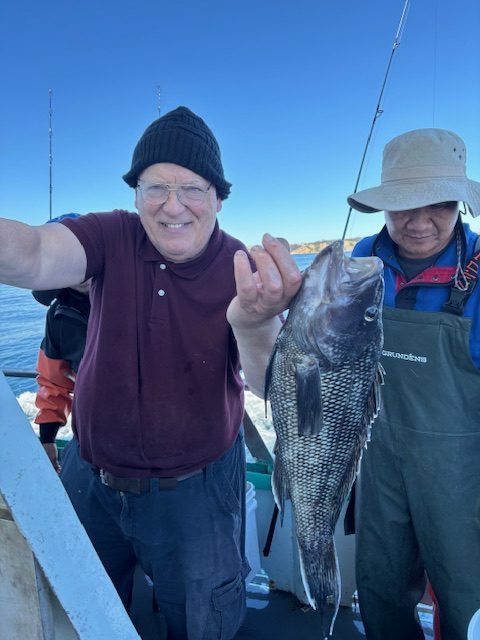 Two men on a boat holding a large fish, with fishing rods visible.