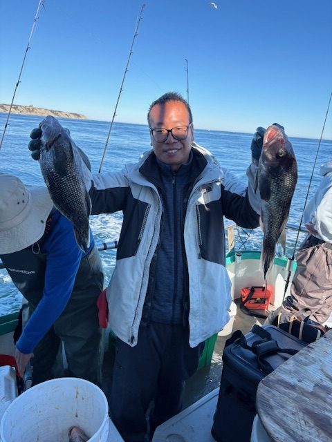 Person smiling, holding two fish on a boat.