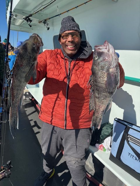 Man in red jacket holds two large fish on a boat.