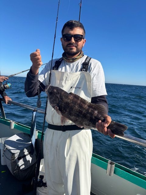 Person in white outfit holding a large fish on a boat with ocean in the background.