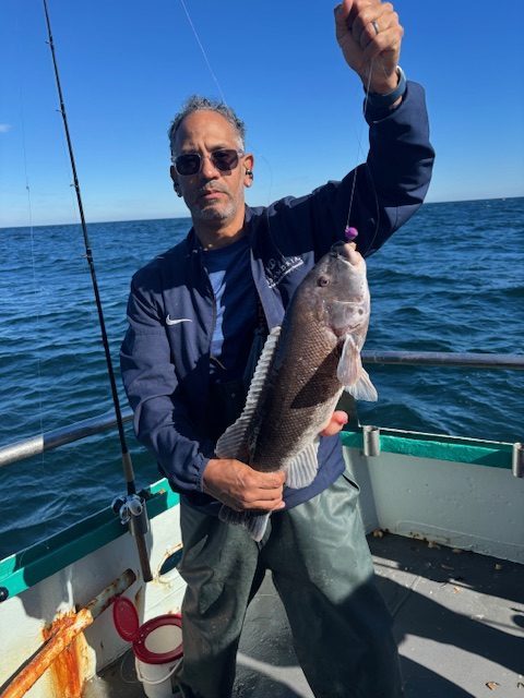Person on boat holding a fish with ocean in background.