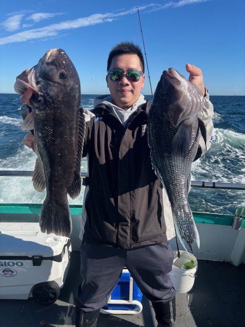 Person on boat holding two large fish with ocean in background.
