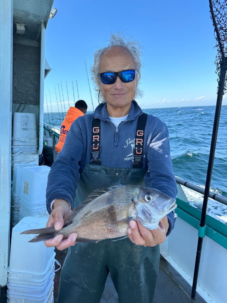 Person holding a fish on a boat at sea, wearing sunglasses and overalls.