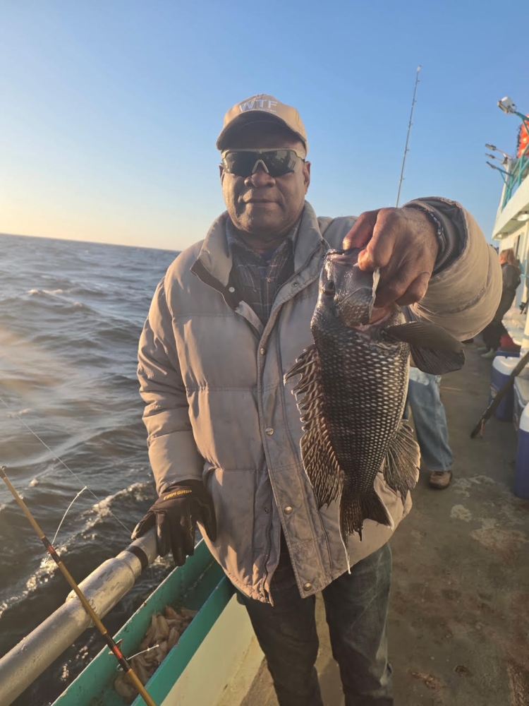 Man in a jacket holding a fish on a boat with ocean in the background.